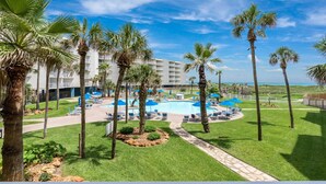 Un resort con area piscina, palme e un edificio bianco con balconi.