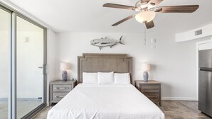 Una camera da letto con un letto, comodini, una ventola a soffitto, un quadro a tema marino e vista panoramica tramite una porta scorrevole in vetro.