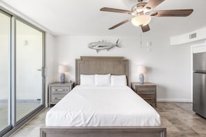 A bedroom with a bed, nightstands, a ceiling fan, a fish wall art, and a view through a sliding glass door. - Sandcastle Condominiums Unit 126 (Port Aransas)