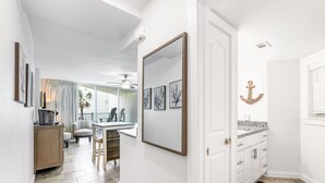 Un corridoio con zona pranzo, una cucina con mobili bianchi e un ampio specchio.