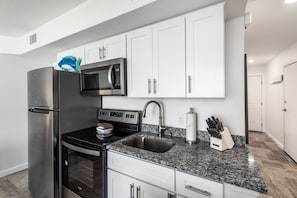 A modern kitchen with white cabinets, stainless steel appliances, a granite countertop, and a built-in microwave. - Sandcastle Condominiums Unit 126 (Port Aransas)
