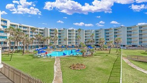 A hotel with multiple balconies, a swimming pool, and palm trees. - Sandcastle Condominiums Unit 135 (Port Aransas)
