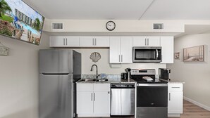 A modern kitchen with white cabinets, stainless steel appliances, and a clock on the wall. - Sandcastle Condominiums Unit 135 (Port Aransas)