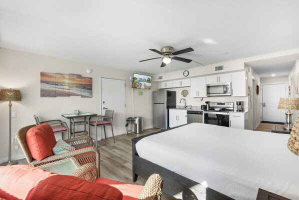 A modern hotel room with a bed, a dining area, a kitchenette, and a TV.