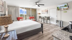 A modern hotel room with a large bed, a dining area, a kitchenette, and a balcony with a view of the landscape. - Sandcastle Condominiums Unit 135 (Port Aransas)