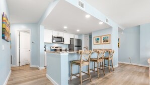 A modern kitchen with white cabinets, a microwave, a refrigerator, and a wooden island with bar stools. - Sandcastle Condominiums Unit 212 (Port Aransas)