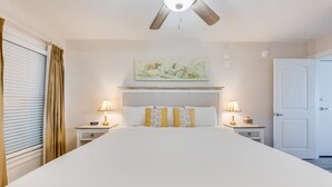 Een hotelkamer met een groot bed, twee nachtkastjes met lampen, een plafondventilator, een deur en een raam met gordijnen.