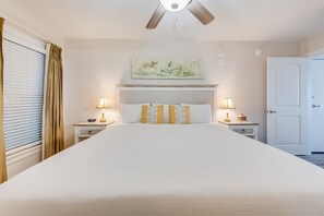Ein Hotelzimmer mit einem großen Bett, zwei Nachttischen mit Lampen, einem Deckenventilator, einer Tür und einem Fenster mit Vorhängen.