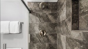 Une salle de bain avec des carreaux de marbre foncé, une douche dotée d’un panneau de commande rond et une serviette blanche suspendue à un porte-serviettes.