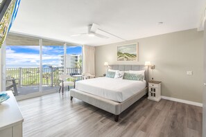 A spacious bedroom with a large bed, a balcony with a view of the city, and a small table with chairs. - Sandcastle Condominiums Unit 315 (Port Aransas)