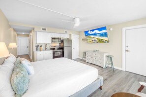 A bedroom with a large bed, a kitchenette, a dining area, and a view of a beach. - Sandcastle Condominiums Unit 315 (Port Aransas)