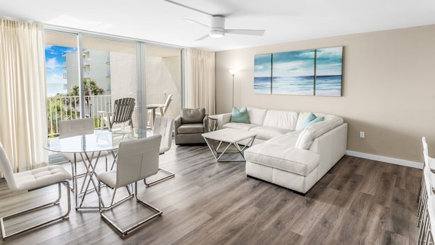 A modern living room with a glass dining table, white sofas, and a ceiling fan. - Sandcastle Condominiums Unit 323 (Port Aransas)