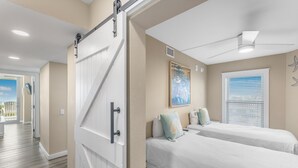 A hotel room with two beds, a sliding door, a ceiling fan, a window with blinds, and a painting on the wall. - Sandcastle Condominiums Unit 323 (Port Aransas)