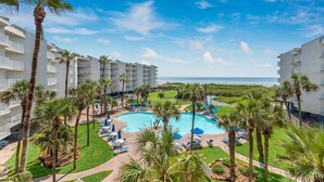 A resort with a central pool surrounded by palm trees and lounge chairs, overlooking the ocean. - Sandcastle Condominiums Unit 323 (Port Aransas)