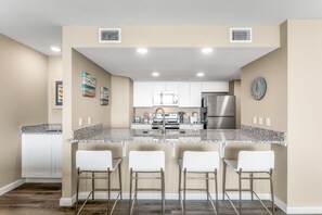 Una cocina moderna con armarios blancos, un refrigerador de acero inoxidable y una encimera de granito.