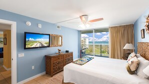 Une chambre dotée d’un grand lit, d’un ventilateur de plafond, d’une télévision et d’un balcon offrant une vue sur l’océan.