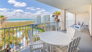 Un balcon avec une table et des chaises blanches, donnant sur une plage et une piscine.