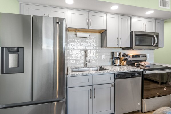 A modern kitchen with stainless steel appliances, grey cabinets, and a tiled backsplash. - Sandcastle Condominiums Unit 427 (Port Aransas)