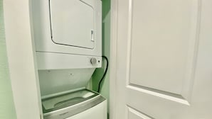 Una lavanderia compatta con lavatrice e asciugatrice a carica frontale, una porta con maniglia argentata e una parete verde.