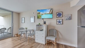 A modern living room with a flat-screen TV, a dining table with chairs, a white cabinet, and framed artwork on the walls. - Sandcastle Condominiums Unit 527 (Port Aransas)