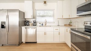 A modern kitchen with stainless steel appliances, white cabinetry, and a window with blinds.