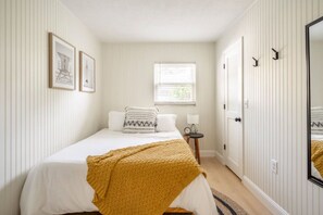 A bedroom with a bed, a window, a bedside table with a lamp, and a mirror on the wall.