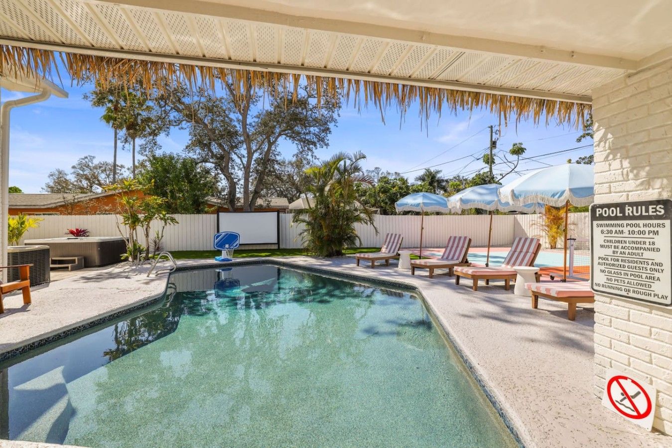 A swimming pool with lounge chairs and a pool rules sign.
