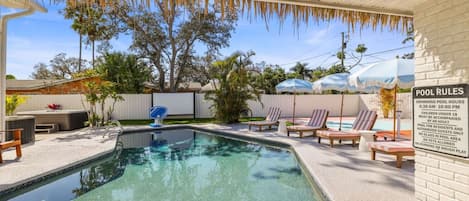 A swimming pool with lounge chairs and a pool rules sign.