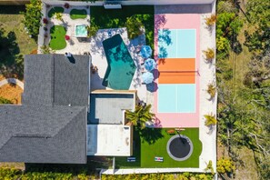 An aerial view of a residential property with a swimming pool, tennis court, and a covered patio area.
