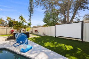 A backyard with a pool, a blue chair, a white screen, and a white fence.
