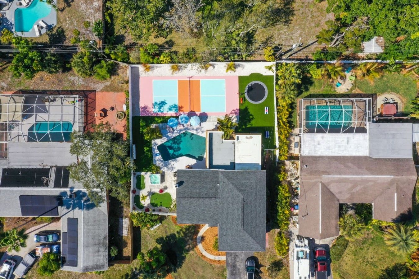 Luchtbeeld van een woonwijk met meerdere huizen, een zwembad in het midden en een tennisbaan.
