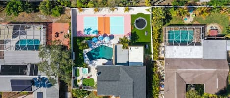 Vista aérea de una zona residencial con varias casas, una piscina central y una cancha de tenis.