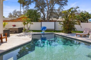 Une piscine avec un jacuzzi, des chaises longues et un panier de basketball, le tout installé dans un jardin.