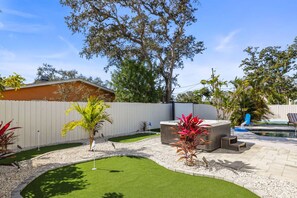 A backyard with a hot tub, artificial grass, and a wooden fence.