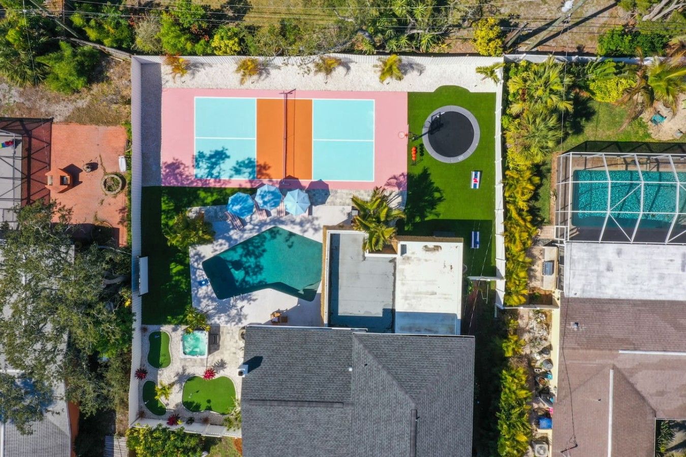 An aerial view of a residential property with a swimming pool, tennis courts, and a landscaped garden.