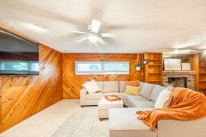 A cozy living room with a sectional sofa, a flat-screen TV, a ceiling fan, and a fireplace.