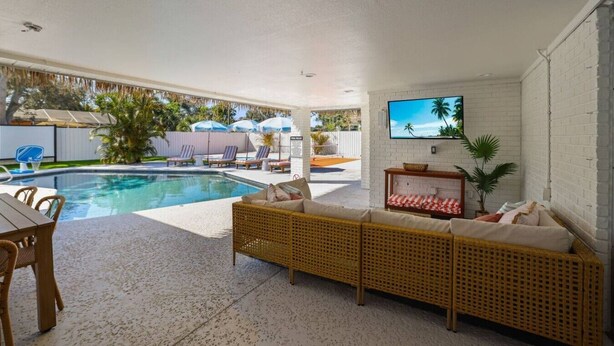 A pool area with a sofa, chairs, and a TV.