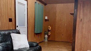 Ein Zimmer mit Holzboden, einem schwarzen Ledersofa mit weißem Kissen, einem grünen Vorhang und einer Vase mit Sonnenblumen.