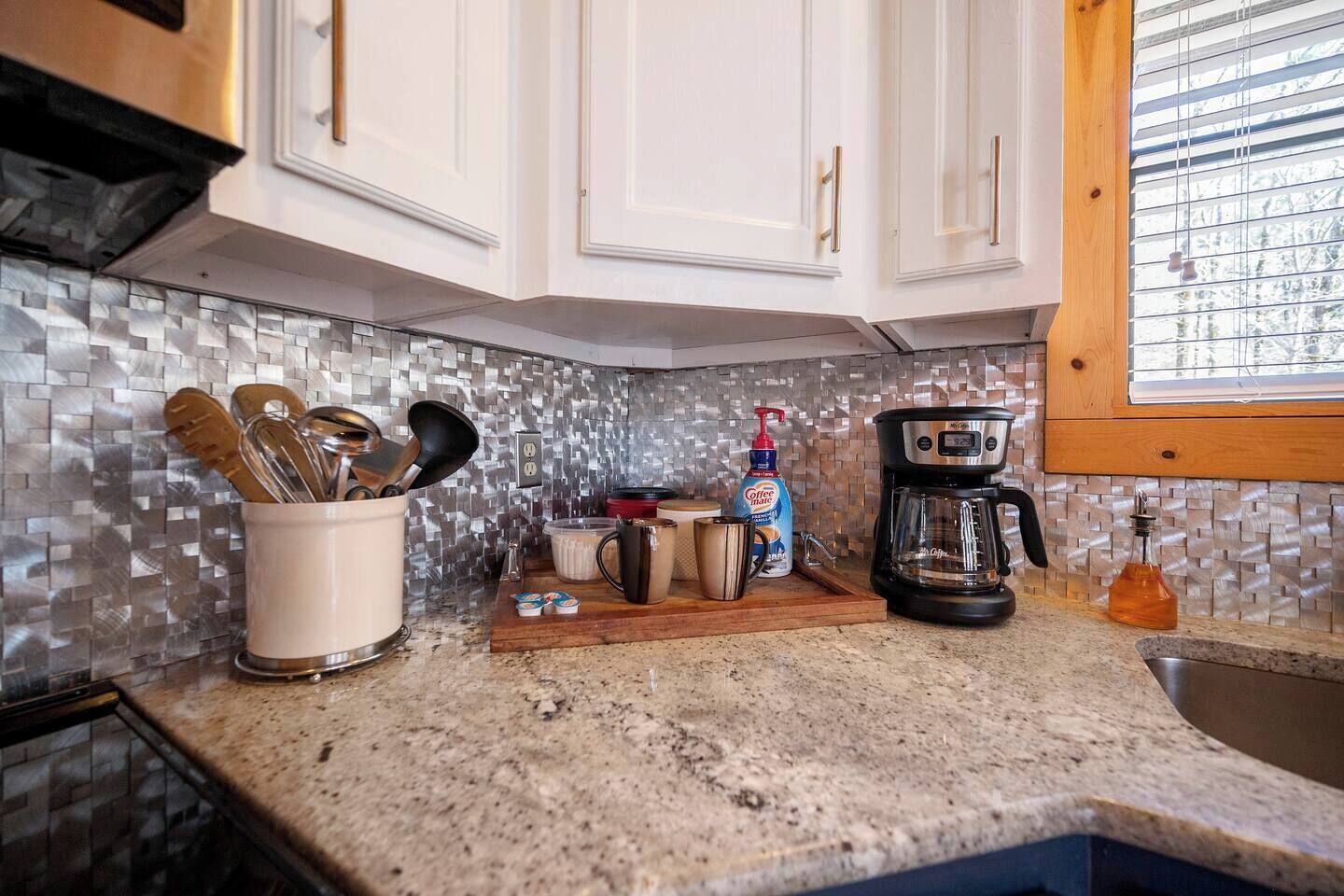 Una cocina con alacenas blancas, una cafetera y una encimera con varios objetos.