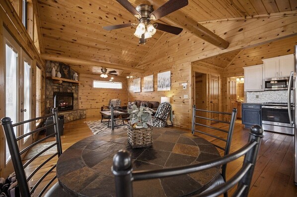 A wooden interior with a stone-tiled dining area, a fireplace, and a kitchen with modern appliances.