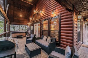A log cabin with a covered porch, outdoor seating area, and a hot tub.