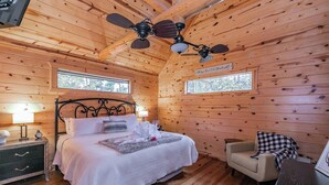 A cozy wooden cabin bedroom with a bed, bedside table, lamp, and a chair. - Secluded Cabin w/ Hot Tub Near State Park (Broken Bow)
