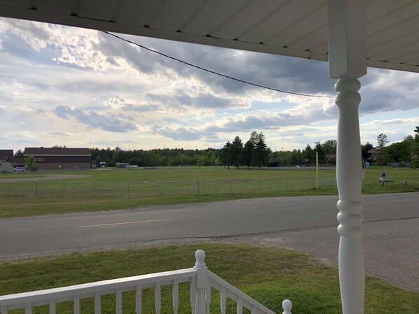 A view from a porch overlooking a grassy field with a fence, a road, and a building in the background. - Central located. Includes finished 2 car garage! 1 minute from beach! (Tawas City)