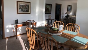 A dining area with a wooden table and chairs, framed artwork on the walls, and a lamp on a side table.