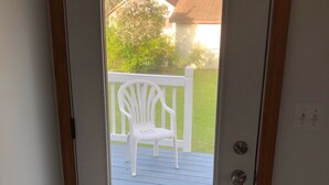 A door leading to a blue wooden deck with a white chair.