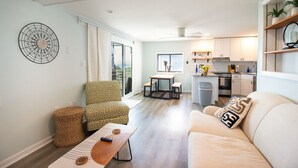 A modern living room with a sofa, a patterned armchair, a dining table, and a kitchen area with white cabinets and a countertop. - #3 Just a few steps from Ocean! Incredible Views! (Carolina Beach)