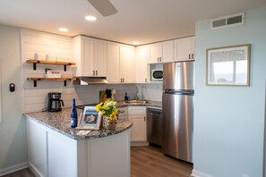 A modern kitchen with white cabinetry, a stainless steel refrigerator, a microwave, and a coffee maker. - #3 Just a few steps from Ocean! Incredible Views! (Carolina Beach)
