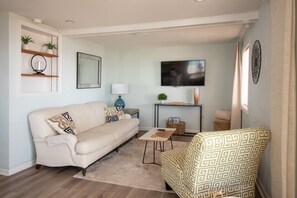 Una sala de estar con un sofá, un sillón estampado, una mesa de centro, un televisor y una mesita auxiliar con una lámpara.