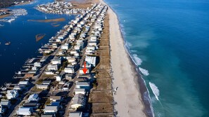 Vue aérienne d’une zone résidentielle côtière, avec des maisons alignées le long de la plage, une marina remplie de bateaux et un océan d’un bleu limpide.