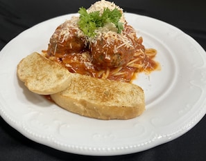 Un plato con dos albóndigas en salsa de tomate, adornado con queso y perejil, acompañado de dos rebanadas de pan tostado.